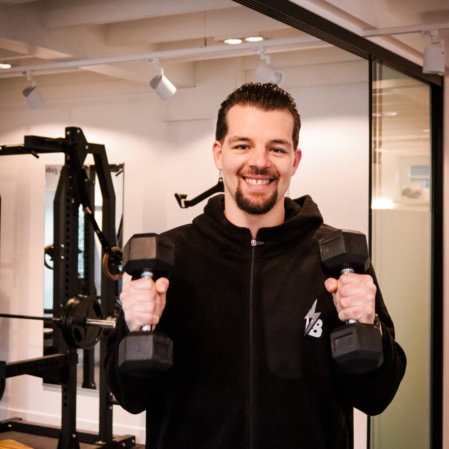 Boaz met een vrolijke uitstraling met twee dumbells in zijn handen, klaar om personal training van hoog niveau te geven.